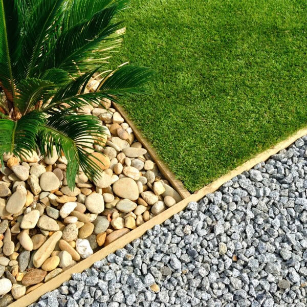 Aerial view of a garden sectioned into three parts: grass, palm tree with stones, and grey gravel.