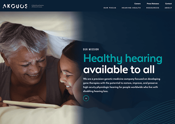 An elderly man and a young girl smiling while looking at a tablet in bed, on a website for a hearing aid company with text about their mission.
