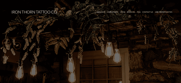 Dimly lit interior of iron thorn tattoo shop featuring exposed light bulbs hanging from the ceiling and lush greenery.