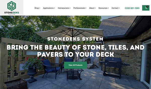 Outdoor patio with stone tiles, pavers, a grill, and seating area under a large umbrella. Text on image: "StoneDeks System - Bring the beauty of stone, tiles, and pavers to your deck".