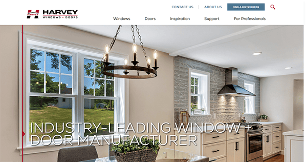 A modern kitchen with large windows, a chandelier, white cabinets, and a stove under a range hood. The text reads "Industry-leading window + door manufacturer." The company name is visible at the top left.