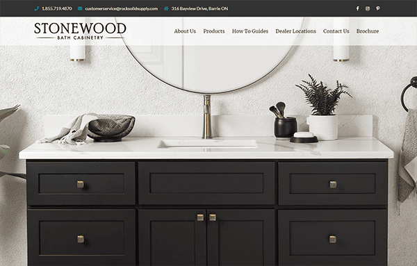 A modern bathroom vanity with black cabinets, white countertop, round mirror, and various decorative items. The image includes contact information and a navigation bar for Stonewood Bath Cabinetry.