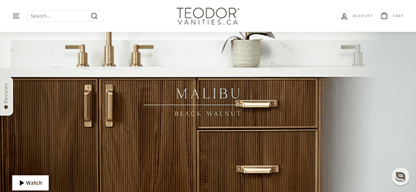 Modern bathroom vanity with wood texture, gold handles and fixtures, and a white countertop, accompanied by a small potted plant. The text "Malibu Black Walnut" is displayed over the image.