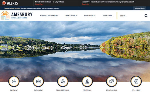 Amesbury, Massachusetts website homepage with a scenic photo of a lake surrounded by trees. Menu options at the bottom include "Pay Online," "Employment," "Trash & Recycling," "City Council," "Report an Issue," and "Get a Permit.