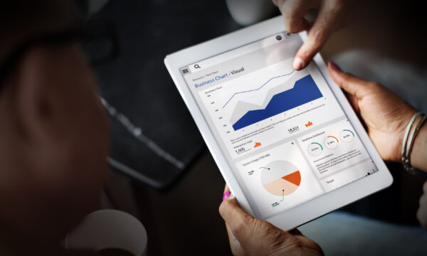 Two individuals, including SEO specialists, review a tablet displaying business charts, featuring a line graph and various pie charts, in a professional setting.