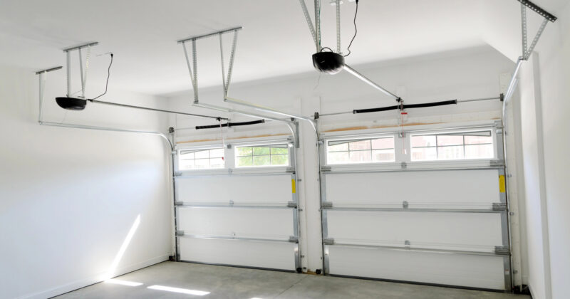 A clean, empty garage with two side-by-side, ceiling-mounted automatic garage doors sourced from one of the best garage door websites, and a concrete floor.