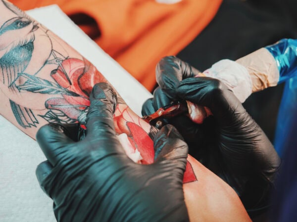 A tattoo artist wearing black gloves is in the process of tattooing a colorful design on a person's arm in one of the busiest tattoo shops around.