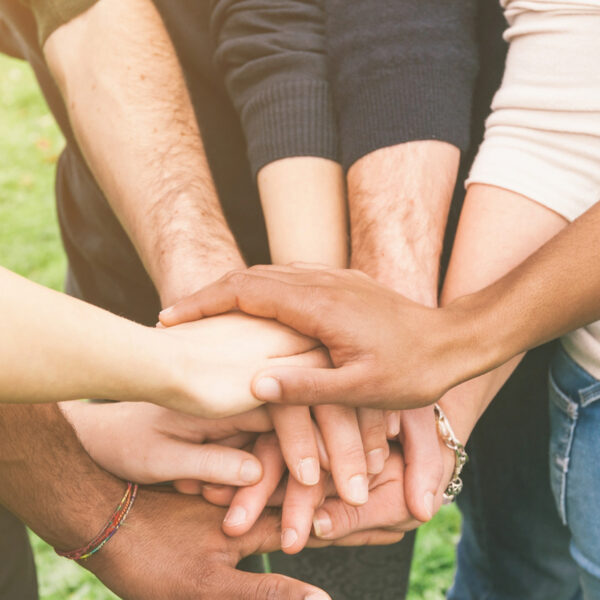 A group of therapists standing in a circle with their hands stacked in the center, symbolizing unity and teamwork.