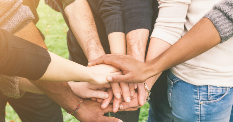 A group of therapists standing in a circle with their hands stacked in the center, symbolizing unity and teamwork.