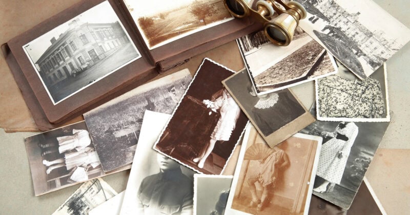 A collection of black and white vintage fashion photographs and a small pair of binoculars are spread out on a table. An open photo album is also visible.