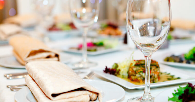 A close-up of a set dining table with neatly folded napkins on plates, several wine glasses, and various dishes in the background highlights the elegance featured on top restaurant websites.