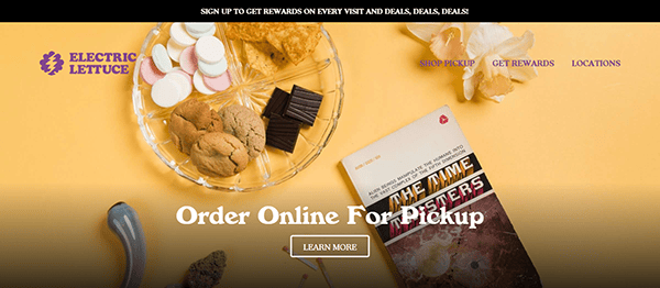 A variety of snacks, including marshmallows, cookies, and chocolate, are displayed on a platter next to a book. Text above reads "Order Online For Pickup" with additional navigation options visible.