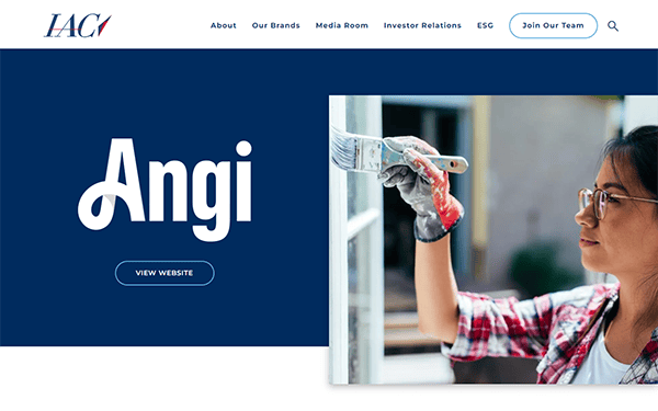 A person in glasses and a plaid shirt paints a window frame with a brush on the Angi brand page of the IAC website.