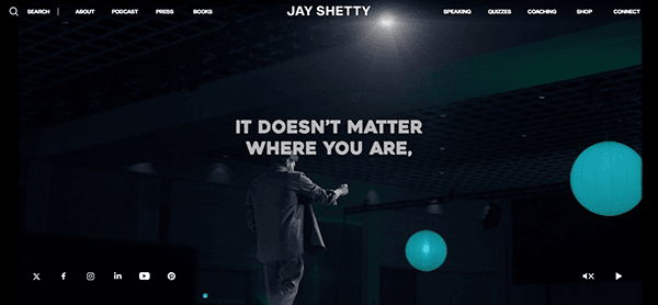 A person on stage in front of a large screen that reads, "It doesn't matter where you are," under the banner "Jay Shetty." The website menu is visible at the top.