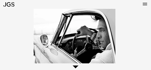 Black and white photo of a man sitting in the driver's seat of a vintage car, looking out of the open window.