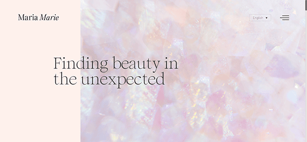 A webpage with a pastel color scheme shows the text "Maria Marie" and "Finding beauty in the unexpected" on a background of iridescent, crystal-like patterns. A language dropdown is present.