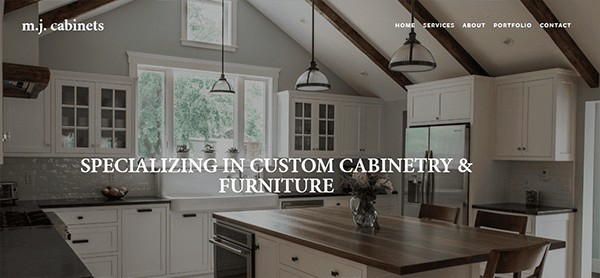 A modern kitchen with white cabinets, a large wooden island, pendant lighting, and a sloped ceiling. Text on image reads "Specializing in Custom Cabinetry & Furniture.