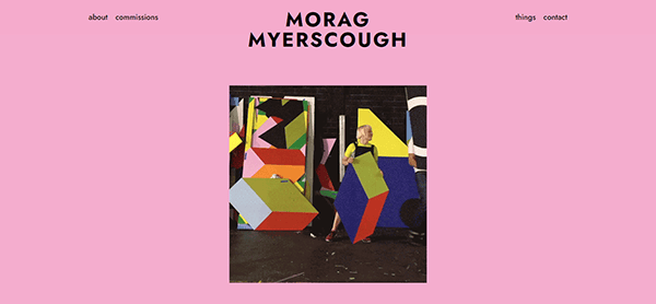 Website with a pink background, displaying the name "Morag Myerscough" at the top and a central image of a person standing among colorful geometric art structures. Navigation links are at the top.