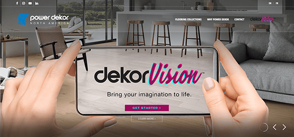 Hands holding a smartphone displaying the Dekor Vision logo and tagline "Bring your imagination to life" in a modern living room with stylish furniture.