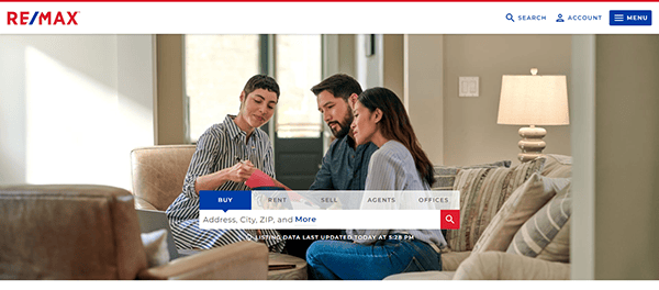 Three people sit on a couch examining documents, with a website search bar at the bottom allowing searches for buying, renting, and selling properties.