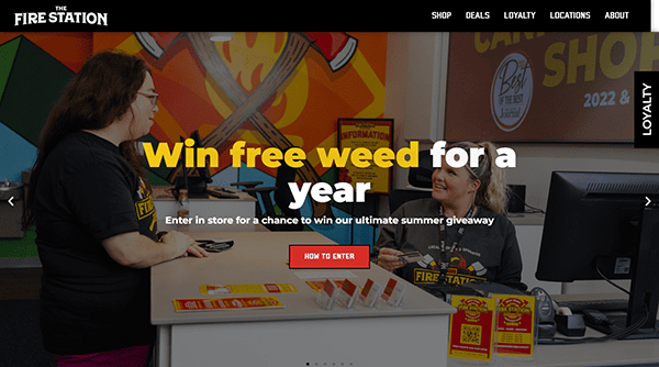 Two employees in a cannabis dispensary converse at a counter promoting a giveaway with the text "Win free weed for a year" prominently displayed.