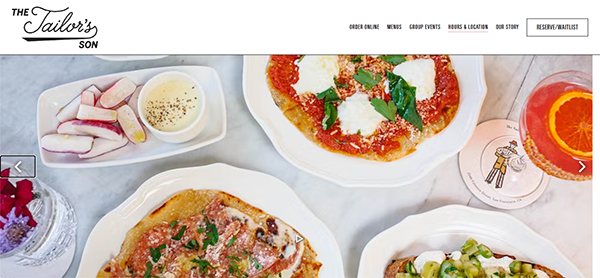 A top-down view of a restaurant table with various dishes including pizzas, a vegetable platter with dip, and a drink. The restaurant’s name, "The Tailor's Son," is visible in the top left corner.