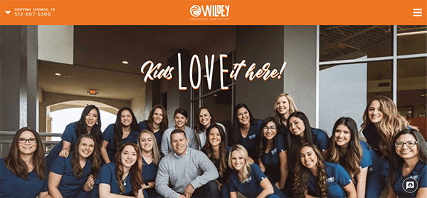 Group photo of the staff of a pediatric dental office with the text "Kids LOVE it here!" on the wall behind them.