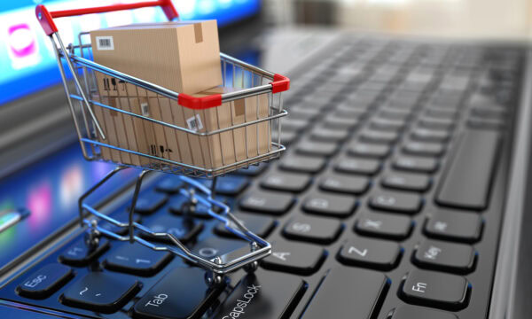 A miniature shopping cart with cardboard boxes rests on a laptop keyboard, illustrating the seamless experience of e-commerce, despite occasional website problems.