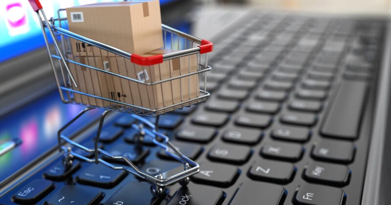 A miniature shopping cart with cardboard boxes rests on a laptop keyboard, illustrating the seamless experience of e-commerce, despite occasional website problems.