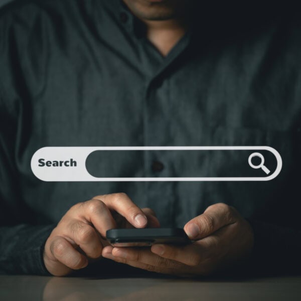 A person in dark clothing uses a smartphone. A search bar graphic with the word "Search" and a magnifying glass icon is superimposed over the image, hinting at SEO audits for improved online visibility.