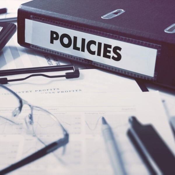 A binder labeled "POLICIES" rests on documents with graphs, next to a calculator, glasses, and pens, ensuring a clear view of privacy considerations.