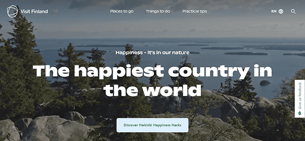 A scenic view of a forested landscape with lakes from a high vantage point is shown on a website titled "Visit Finland," with the slogan "The happiest country in the world" displayed prominently.