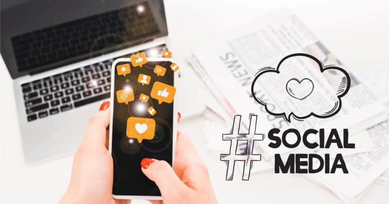 A person is using a smartphone, with social media icons dynamically floating above the screen. A laptop and newspapers lie in the background, while "Social Media" with a cloud and hashtag appears on the right, highlighting psychology-based principles for better engagement.