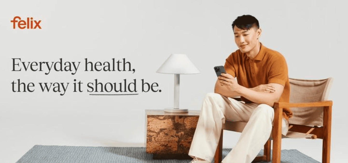 A person in a brown shirt sits on a wooden chair, scrolling through examples of winning social media ads on their phone. A lamp glows softly on the table beside them. The wall reads, "Everyday health, the way it should be.