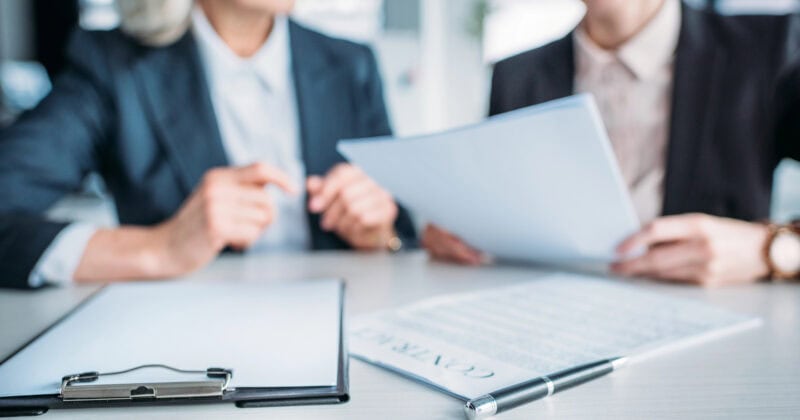 Two people review documents at a table, offering an overview of strategies for business growth, with a clipboard and pen in the foreground.