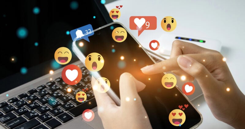 A person using a smartphone next to a laptop is immersed in social media marketing. Various reaction icons hover above the phone's screen, reflecting their engagement with proven strategies to boost online presence.