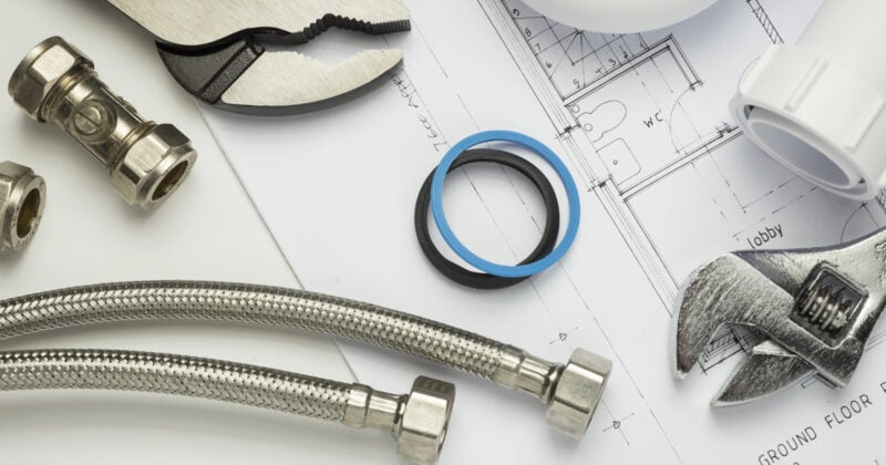 Expert tips and quality plumbing tools come together on architectural plans, showcasing essential pliers, wrenches, pipes, and a rubber gasket.