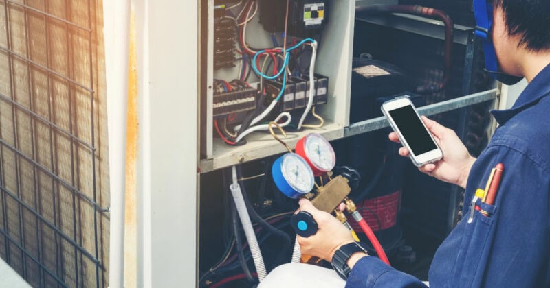 A technician expertly checks the HVAC system using gauges and a smartphone, ready to address any customer calls with precision.