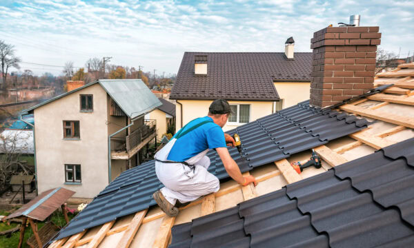 A worker installs metal roofing sheets on a residential roof under a partly cloudy sky, expertly meeting contractor needs. The project incorporates elements that are crucial for converting leads, inspired by innovative roofing website design principles.