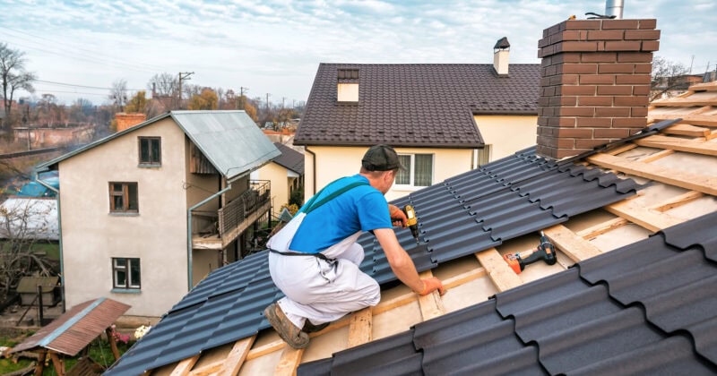 A worker installs metal roofing sheets on a residential roof under a partly cloudy sky, expertly meeting contractor needs. The project incorporates elements that are crucial for converting leads, inspired by innovative roofing website design principles.