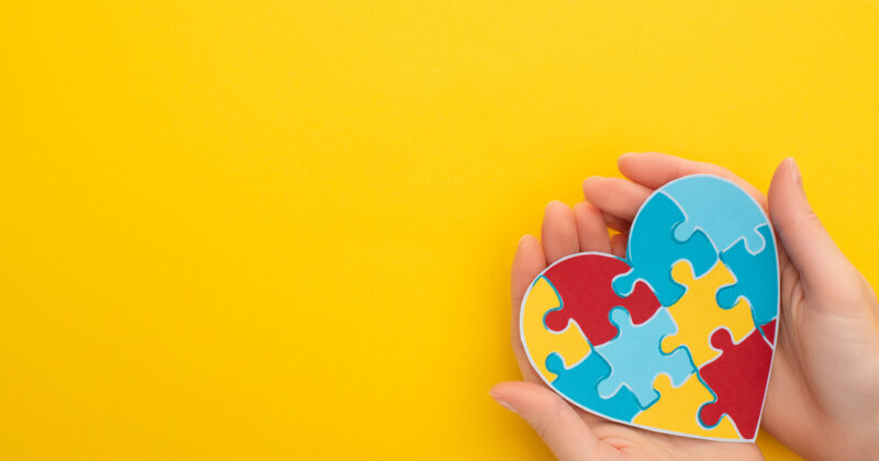 Hands holding a heart-shaped puzzle made of colorful pieces against a yellow background, symbolizing the vibrant unity and connection found in charity website designs.