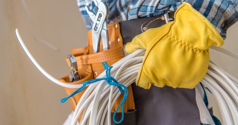 A person wearing gloves holds a bundle of cables and tools in a tool belt, including a wrench, ready to tackle any HVAC challenge.