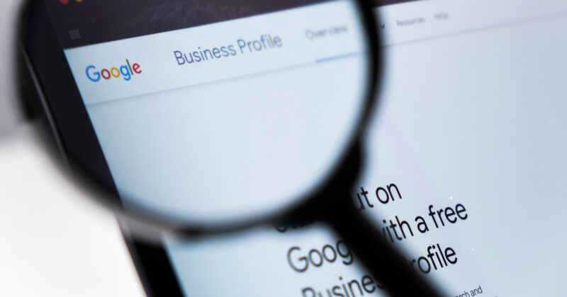 A magnifying glass focuses on a computer screen displaying the Google Business Profile webpage, highlighting its various categories to optimize business visibility.