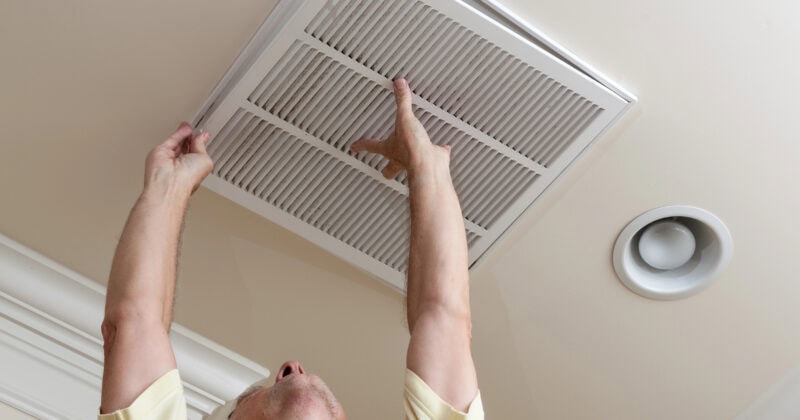 Person in a yellow shirt reaching up to adjust a ceiling vent in an HVAC-equipped room.