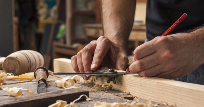 Close-up of a person meticulously marking a wooden plank with a pencil and ruler on a workbench, surrounded by wood shavings and tools—a scene that could grace the homepage of the best carpenter websites.