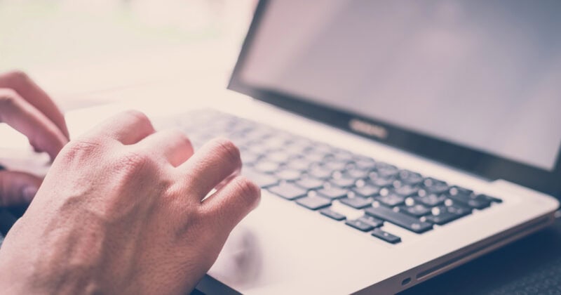 A person types on a laptop with a black keyboard and silver casing, carefully focusing on the left side of the keyboard, highlighting accessibility features.