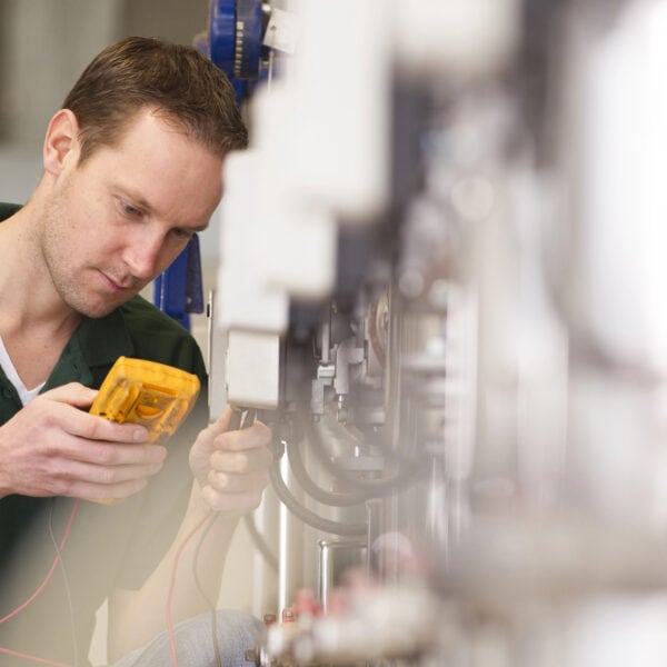 An electrician in a green shirt expertly uses a multimeter to test electrical equipment in an industrial setting.