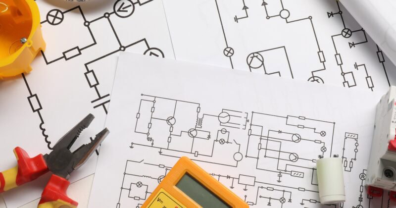 Electrical diagrams, pliers, a multimeter, and wiring are neatly arranged on the table—a quintessential setup for skilled electricians.