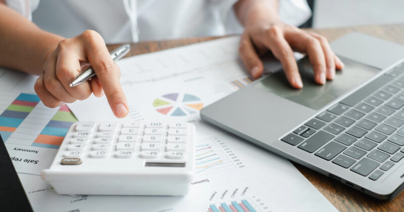 An accountant navigates their laptop and calculator amid financial charts and graphs, potentially inspired by layouts from some of the best accountant websites.