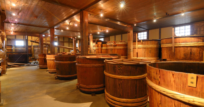 A wooden room housing several large wooden fermentation barrels, akin to the cozy interiors admired on the best brewery websites, is warmly lit by ceiling lights.